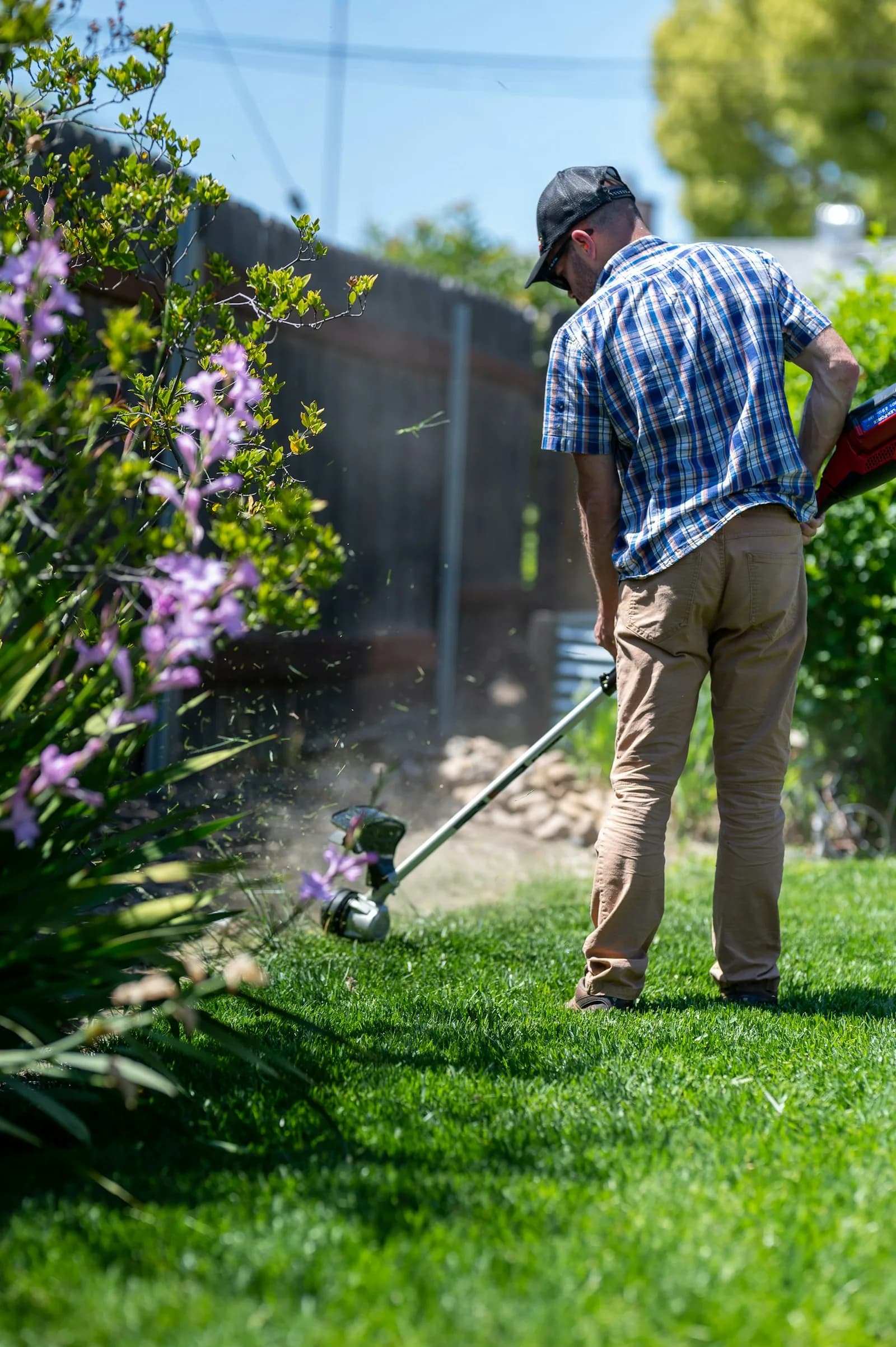 A landscaper using a string trimmer along a planted border